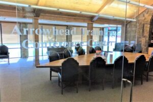 A large table shaped like an arrowhead, that is surrounded by black chairs, behind a glass door that reads "Arrowhead Training Conference Center"