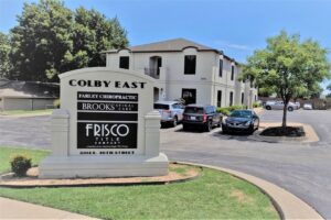 The outside of the Frisco Title Company building behind a sign that says "Colby East; Farley Chiropractic, Brooks Spinal Care, Frisco Title Company"