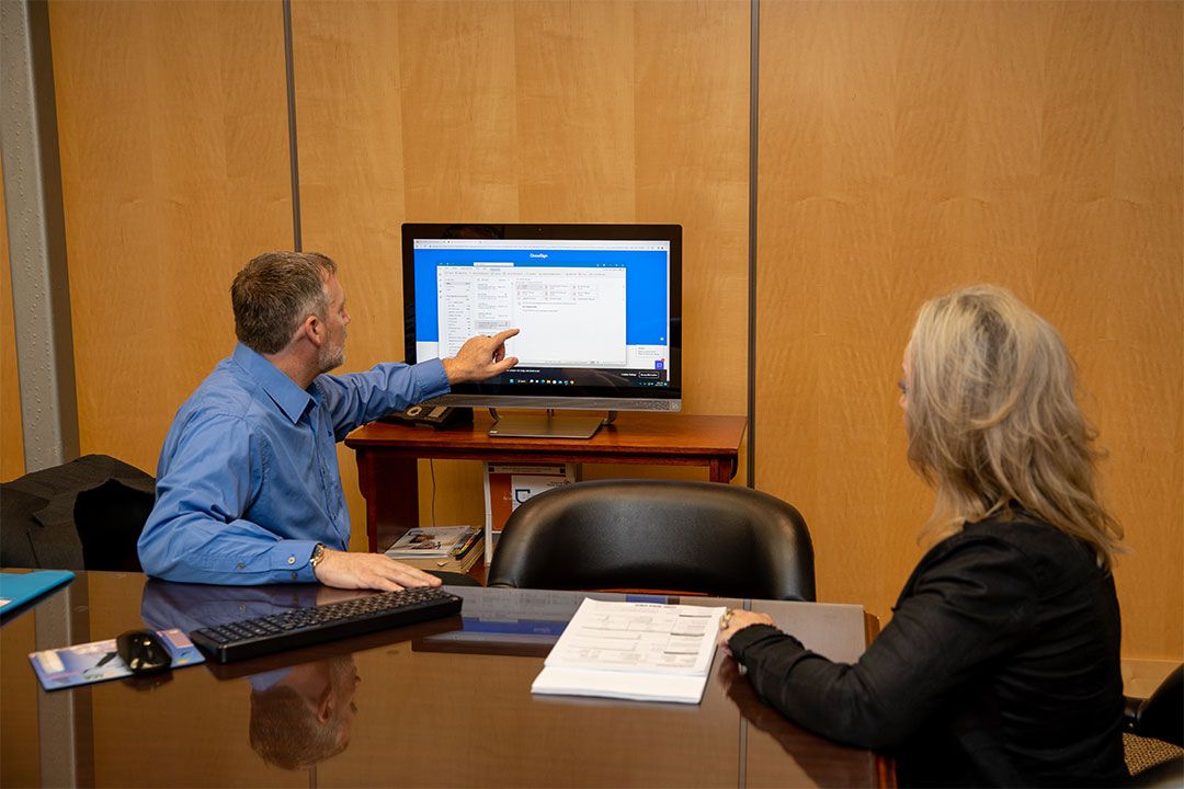 A woman watches a man pointing at a computer screen providing abstracting services