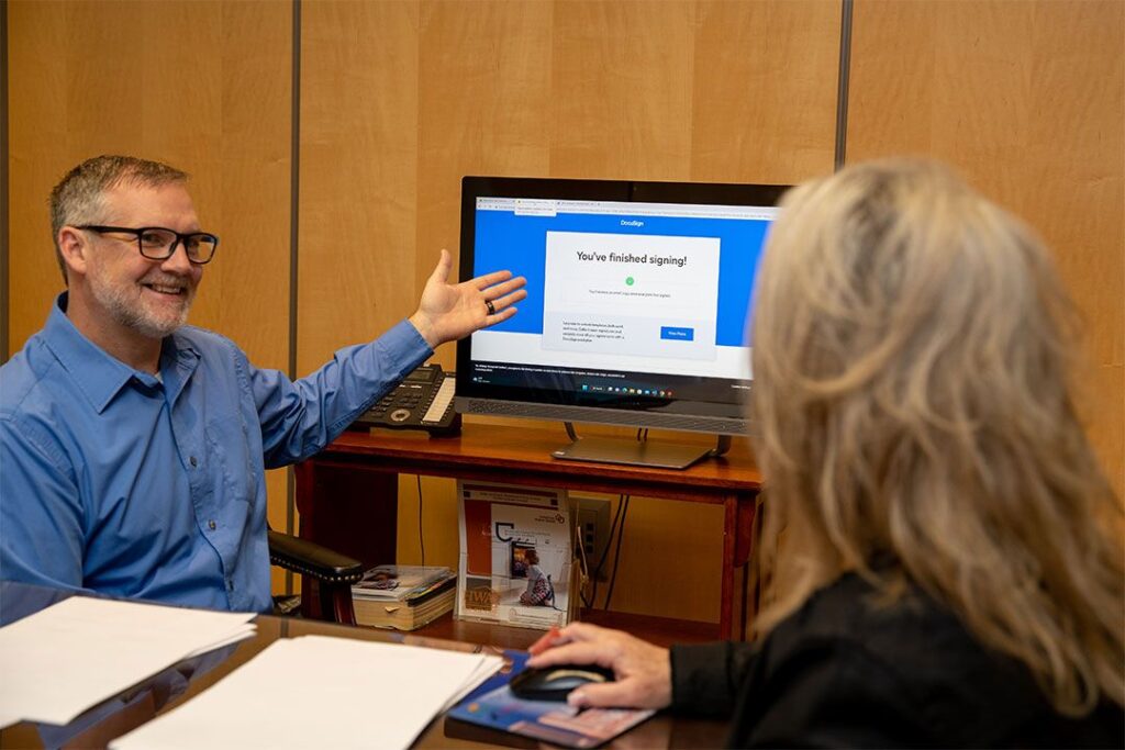 A smiling man shows a woman a computer screen that reads "you've finished signing!"