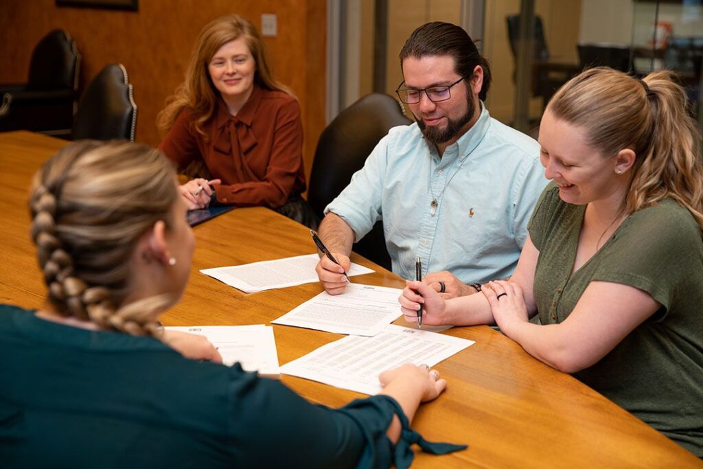 A group of people sign paperwork at a large table.