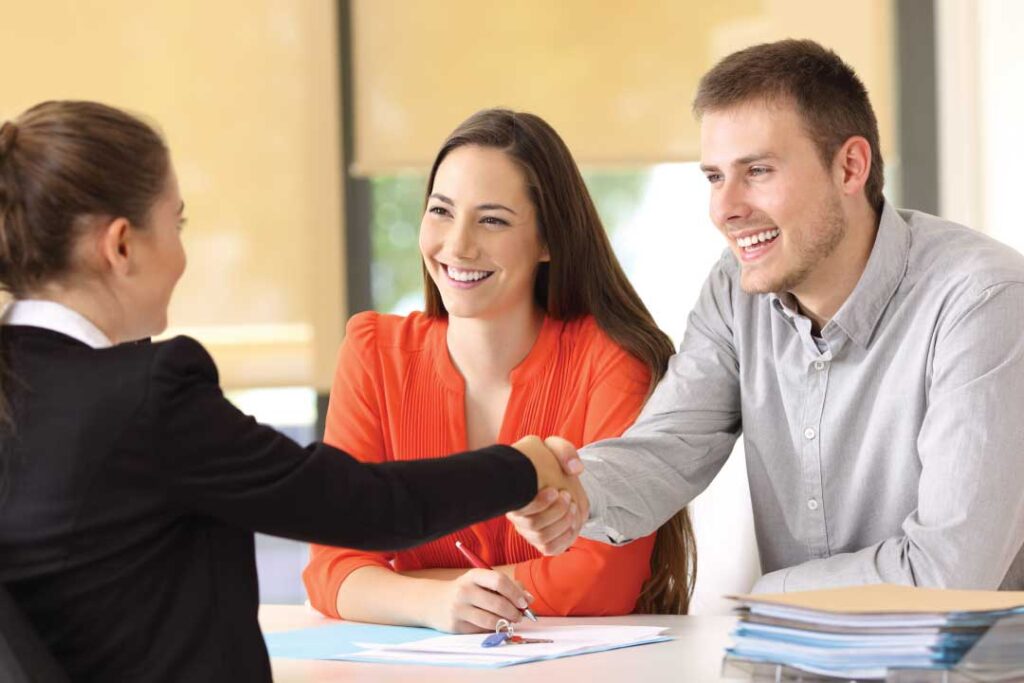 Young couple shaking hands and signing contract with an agent