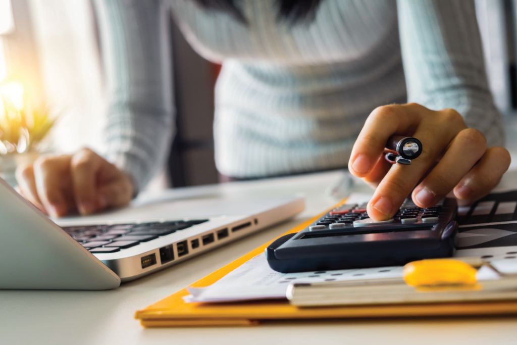 ladys hands using a calculator and laptop at her desk